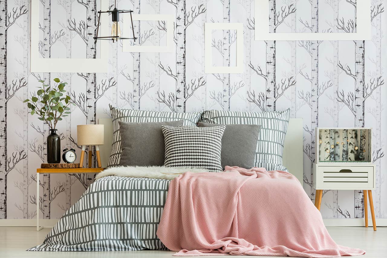 Feminine bedroom interior with forest inspired wallpaper and geometric bedding